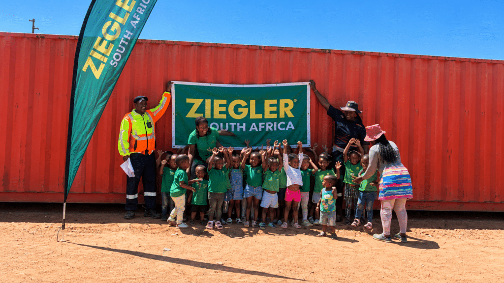 Children and adults in front of a donated shipping container, holding a Ziegler South Africa banner.